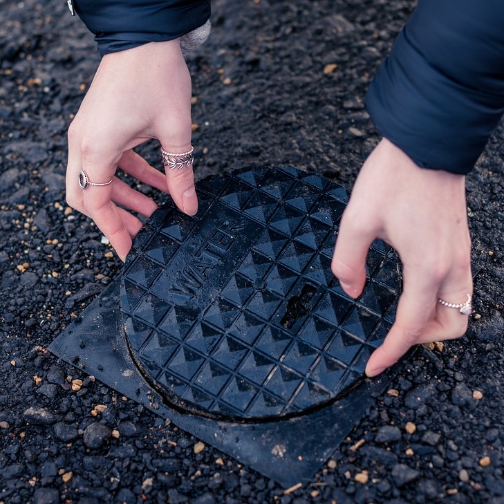 hands opening a water meter chamber in footpath