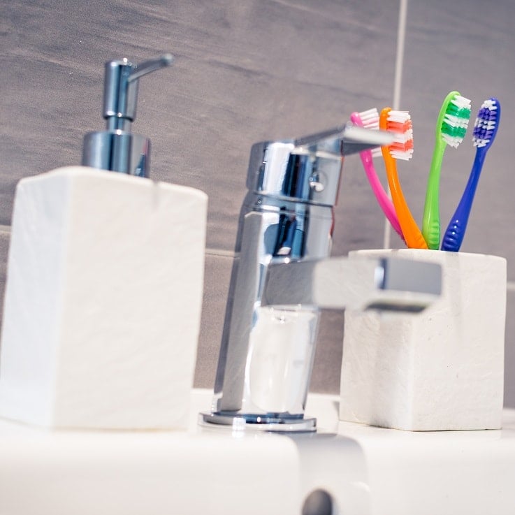 toothbrushes in holder next to tap