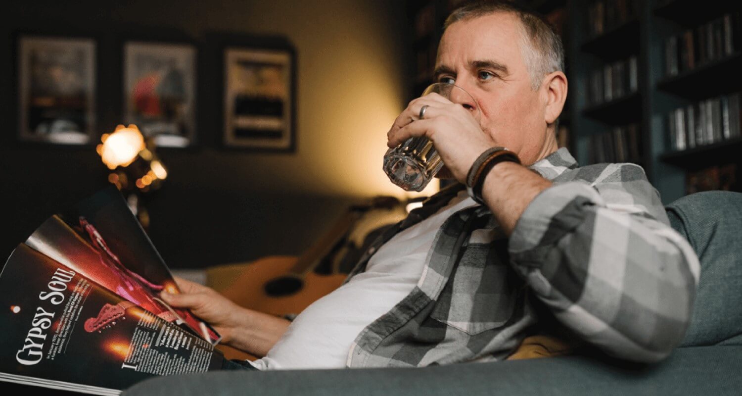 Man on sofa with a magazine drinking a glass of water