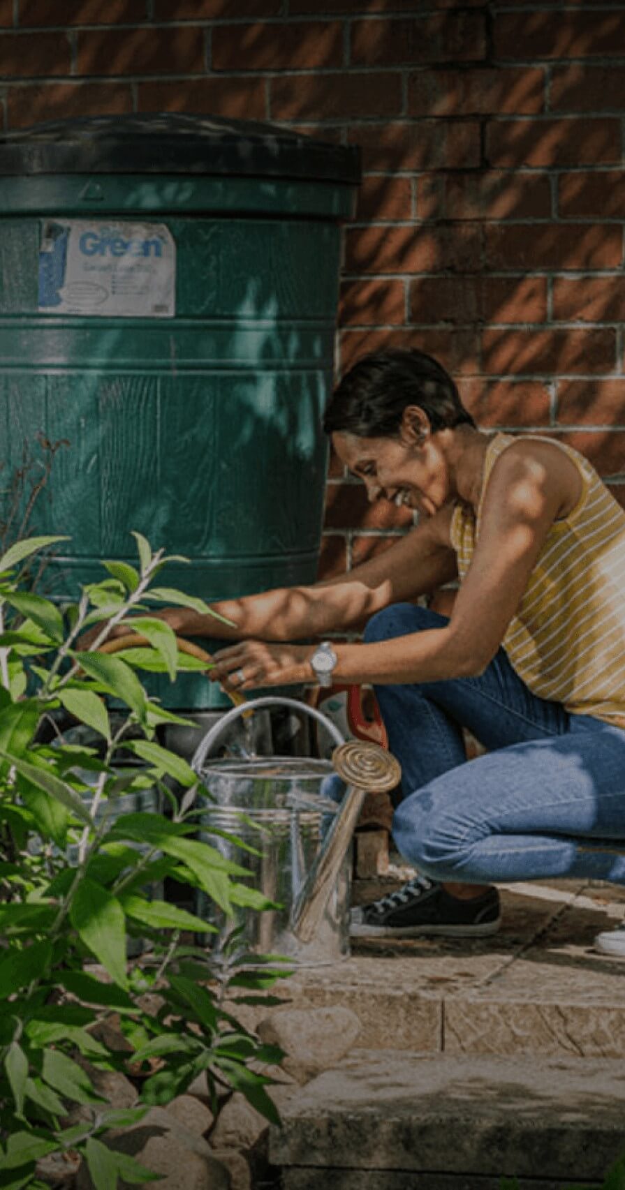Woman filling watering can from a water butt