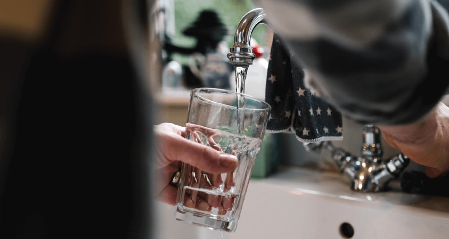 Someone filling up a glass with tap water in the kitchen